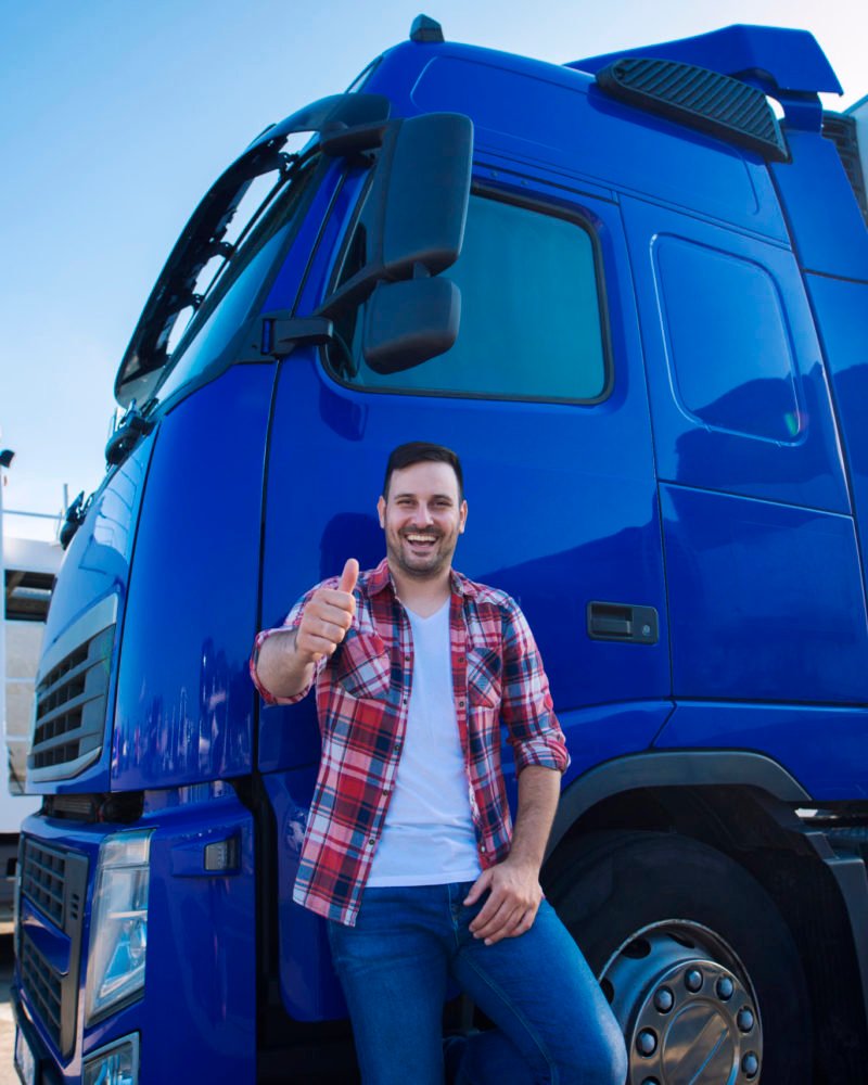 Professional truck driver in front of long transportation vehicle holding thumbs up ready for a new ride.